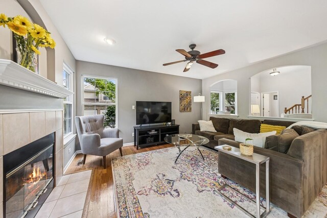 6173 Dixon Dr, Lisle, IL 60532 - living room with a tiled fireplace, light wood-type flooring, ceiling fan, arched walkways, and baseboards
