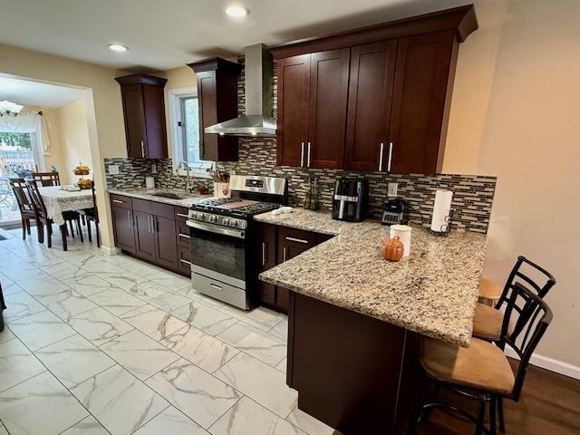 431 Edward St, Sycamore, IL 60178 - kitchen with gas stove, wall chimney exhaust hood, a sink, a breakfast bar, and a peninsula