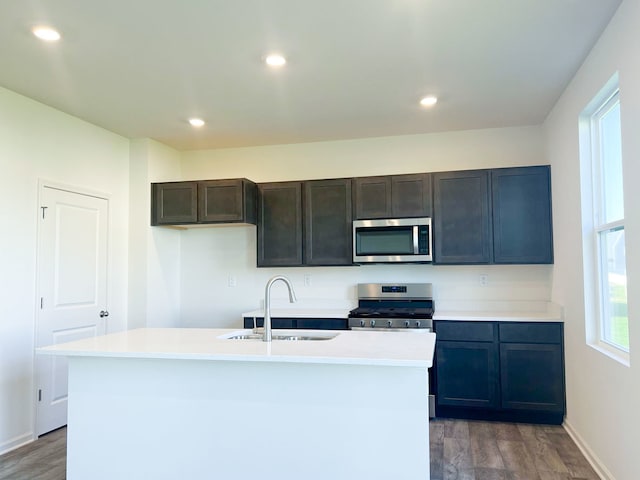 kitchen with appliances with stainless steel finishes, a sink, wood finished floors, light countertops, and baseboards