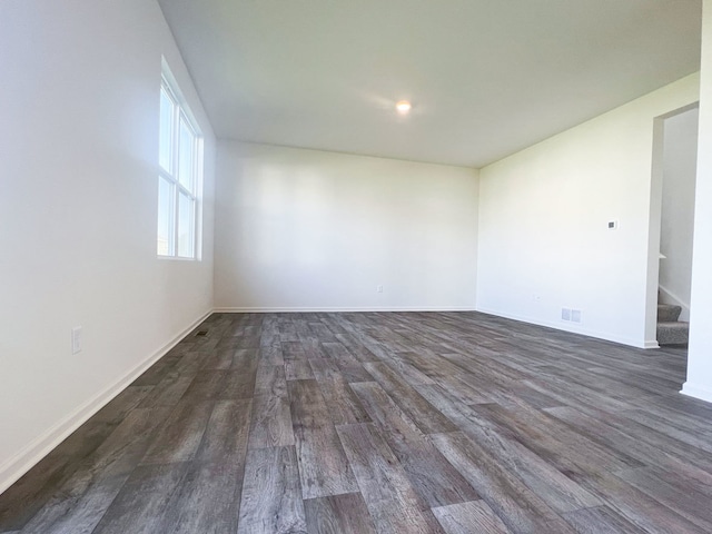 spare room featuring dark wood-style flooring, stairs, and baseboards
