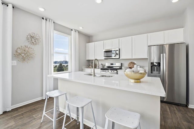kitchen featuring appliances with stainless steel finishes, a sink, dark wood-type flooring, a kitchen breakfast bar, and recessed lighting