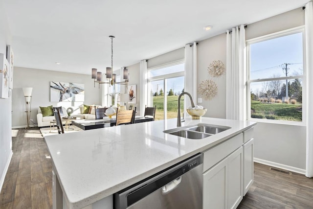 kitchen featuring stainless steel dishwasher, a sink, a center island with sink, and baseboards