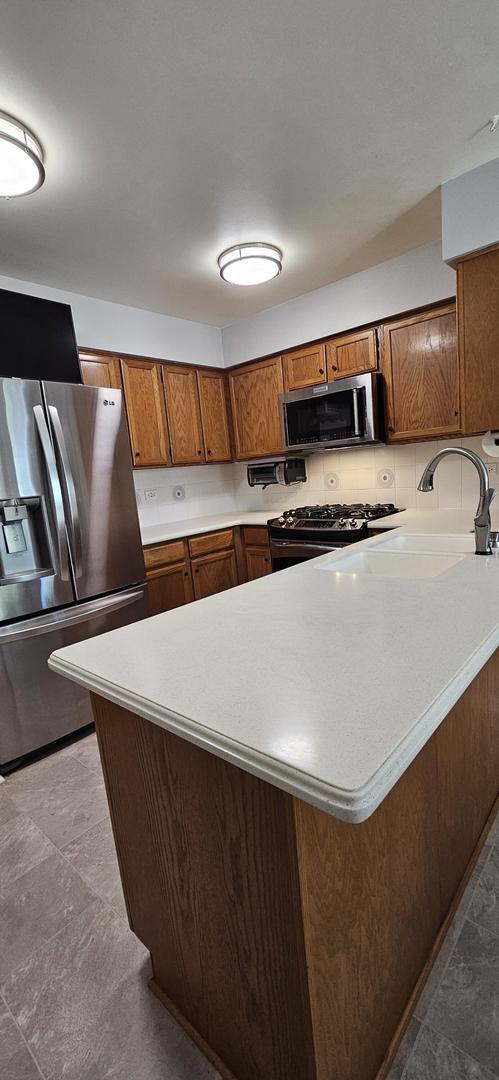 973 Willowbrook Dr, Wheeling, IL 60090 - kitchen featuring appliances with stainless steel finishes, brown cabinets, light countertops, a sink, and a peninsula
