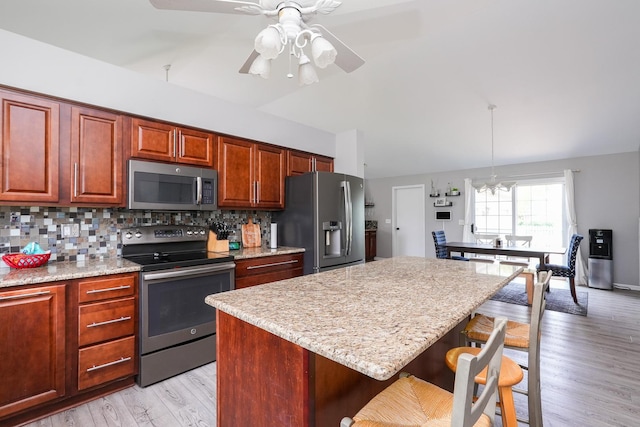 413 W Cook St, Manteno, IL 60950 - kitchen featuring appliances with stainless steel finishes, a breakfast bar, tasteful backsplash, a kitchen island, and light stone counters