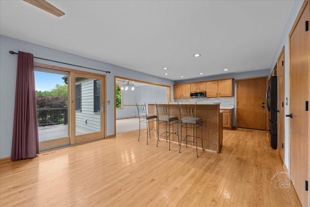 10N738 Prairie Xing, Elgin, IL 60124 - kitchen featuring stainless steel microwave, freestanding refrigerator, a breakfast bar, light wood-style flooring, and a peninsula