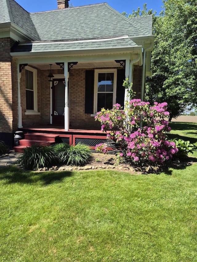 123 W Maple St, Franklin Grove, IL 61031 - property entrance with covered porch, a chimney, brick siding, and a yard