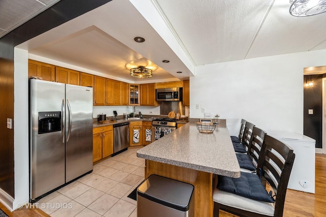 914 N Austin Blvd Unit B10, Oak Park, IL 60302 - kitchen featuring appliances with stainless steel finishes, a peninsula, brown cabinetry, a kitchen breakfast bar, and glass insert cabinets