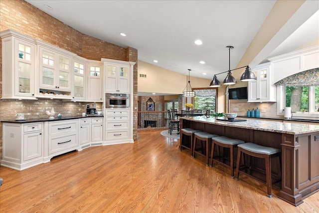 10348 Woburn Ct, Orland Park, IL 60462 - kitchen featuring light wood finished floors, tasteful backsplash, a kitchen breakfast bar, high vaulted ceiling, and white cabinetry