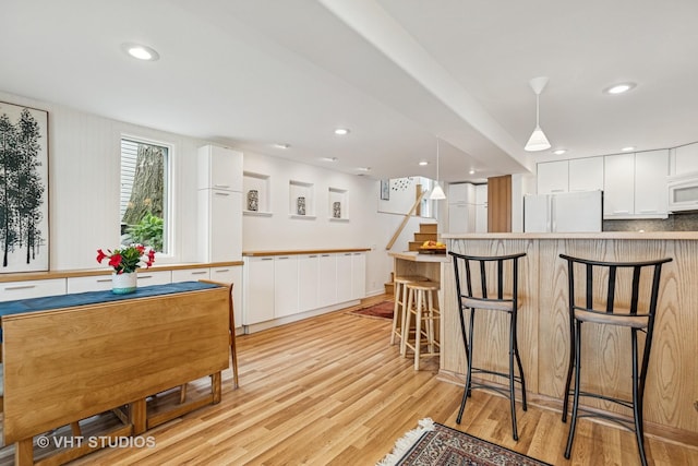 18 N Lake Ave, Fox Lake, IL 60020 - kitchen featuring white appliances, white cabinetry, a kitchen bar, light wood-style flooring, and pendant lighting