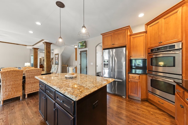 12923 Grande Pines Blvd, Plainfield, IL 60585 - kitchen featuring appliances with stainless steel finishes, decorative columns, a center island, light stone counters, and dark wood-type flooring