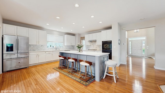 296 Huron St, Vernon Hills, IL 60061 - kitchen with stainless steel fridge, a kitchen breakfast bar, light wood-type flooring, white cabinets, and tasteful backsplash