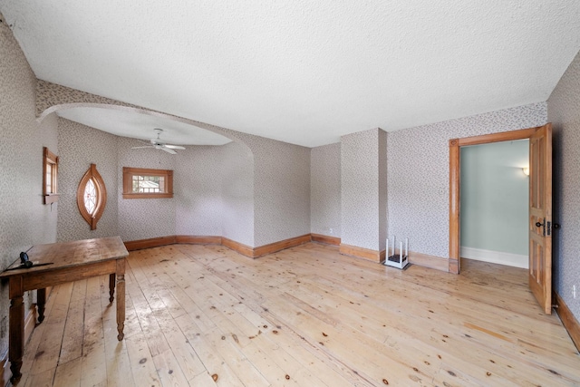 508 Grant St, Earlville, IL 60518 - empty room featuring arched walkways, light wood-style flooring, wallpapered walls, ceiling fan, and a textured ceiling