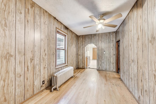 7649 S Dobson Ave, Chicago, IL 60619 - empty room featuring radiator, arched walkways, ceiling fan, wood finished floors, and wooden walls