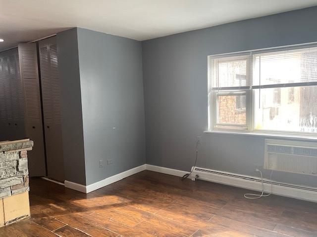 7854 S S Shore Dr Unit 306, Chicago, IL 60649 - empty room with baseboards, wood finished floors, a wall unit AC, and a baseboard radiator