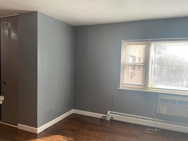7854 S S Shore Dr Unit 306, Chicago, IL 60649 - spare room featuring baseboard heating, dark wood finished floors, baseboards, and a wall mounted air conditioner