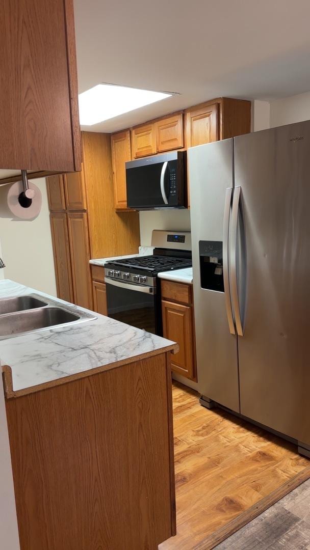 kitchen with stainless steel appliances, light wood finished floors, light countertops, and brown cabinets