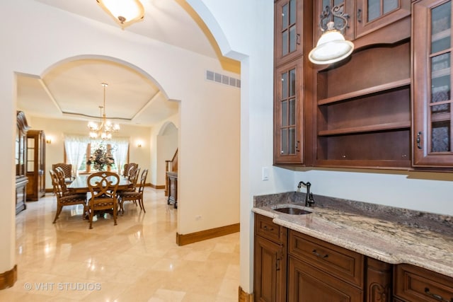10944 Arbor Ridge Dr, Orland Park, IL 60467 - kitchen featuring arched walkways, light stone counters, decorative light fixtures, a raised ceiling, and glass insert cabinets
