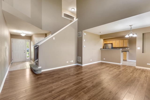 453 Lancaster Dr, Pingree Grove, IL 60140 - unfurnished living room featuring light wood-style flooring, baseboards, a high ceiling, a chandelier, and stairs