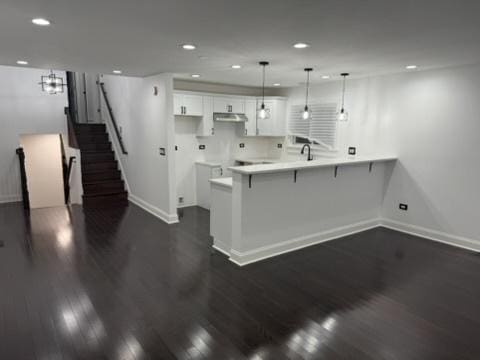 6903 S Ada St, Chicago, IL 60636 - kitchen featuring baseboards, under cabinet range hood, a breakfast bar, a peninsula, and dark wood-style floors