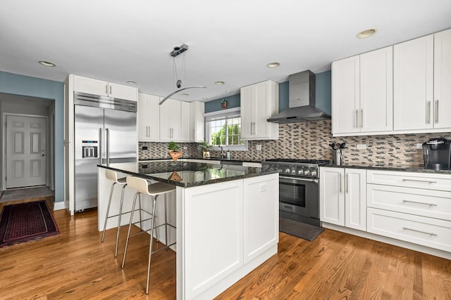 1101 Oak St, Winnetka, IL 60093 - kitchen featuring wall chimney range hood, high quality appliances, a kitchen bar, a kitchen island, and white cabinetry