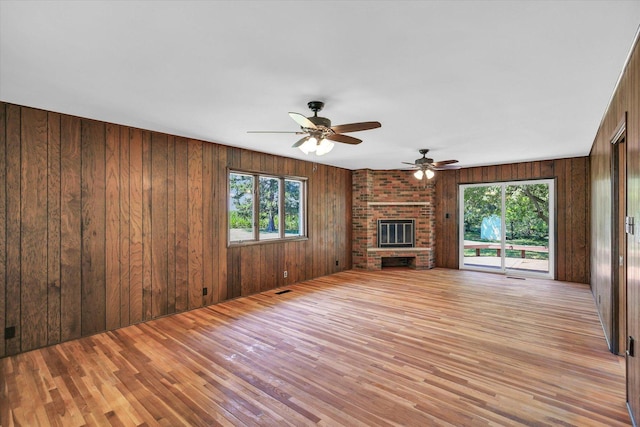 1651 Phillips Woods Ln, Urbana, IL 61802 - unfurnished living room with healthy amount of natural light, light wood-type flooring, wood walls, a ceiling fan, and a brick fireplace