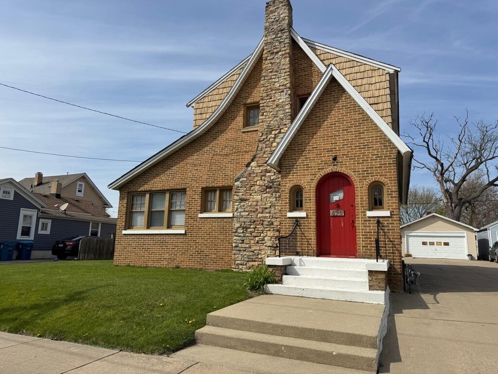 610 E Benton St, Aurora, IL 60505 - tudor home with a garage, an outdoor structure, a front yard, brick siding, and a chimney
