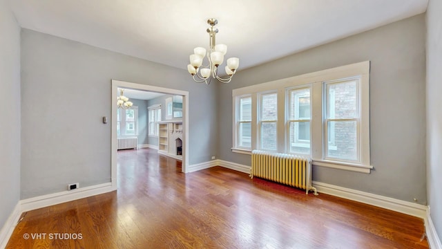 7832 S Paxton Ave, Chicago, IL 60649 - empty room with radiator heating unit, a chandelier, wood finished floors, and a fireplace
