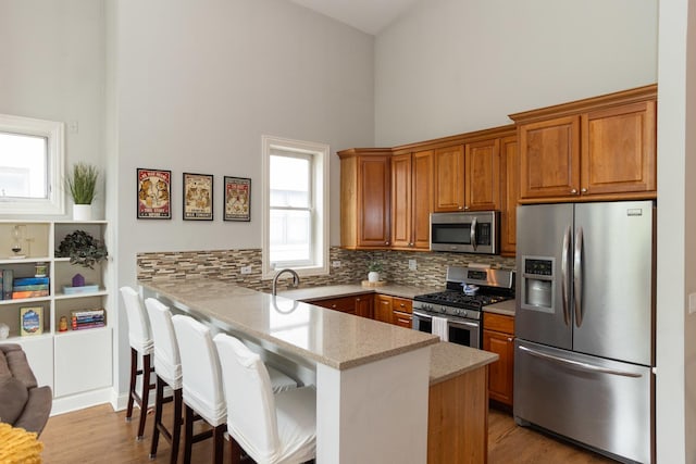 4541 N Malden St Unit 3N, Chicago, IL 60640 - kitchen with stainless steel appliances, a peninsula, a towering ceiling, brown cabinetry, and decorative backsplash