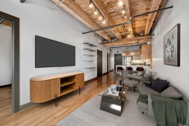 living room with wood ceiling with exposed beams, wood finished floors, track lighting, and baseboards
