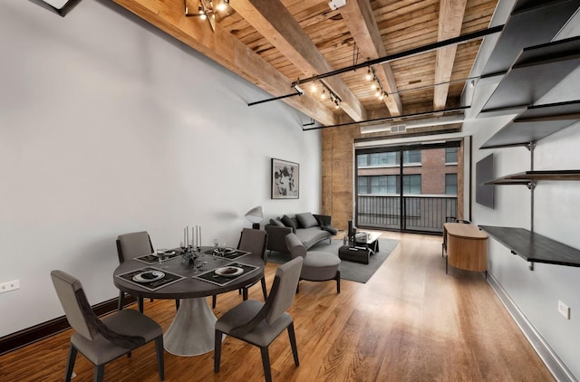 dining area with wooden ceiling with exposed beams, wood finished floors, track lighting, baseboards, and a high ceiling