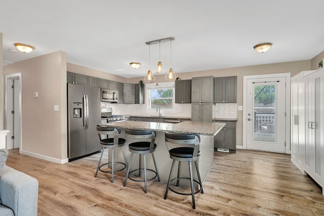 710 Sunset Ln, Shorewood, IL 60404 - kitchen featuring stainless steel appliances, gray cabinets, backsplash, a kitchen bar, and light wood-style floors