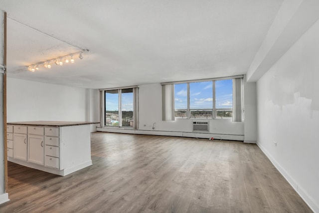 8801 W Golf Rd Unit 10C, Niles, IL 60714 - unfurnished living room with wood finished floors, rail lighting, baseboards, and a wall mounted air conditioner