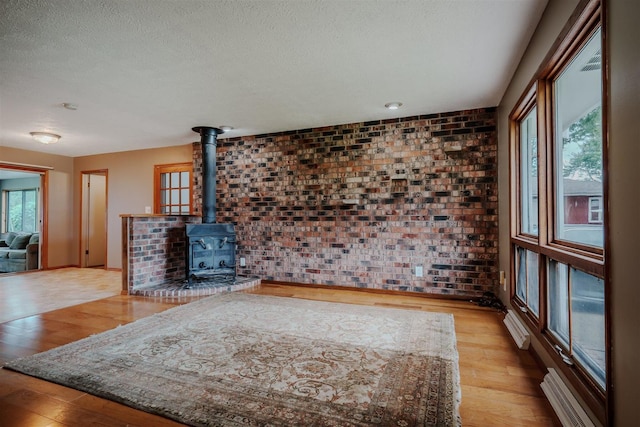 20541 E 2050 N Rd, Towanda, IL 61776 - unfurnished living room featuring brick wall, a wood stove, wood finished floors, a textured ceiling, and a baseboard radiator