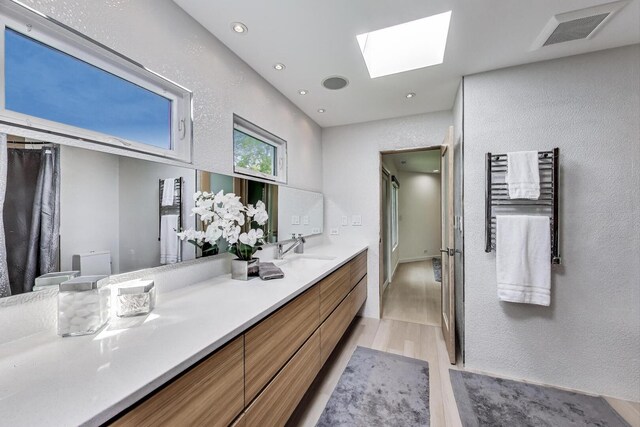 870 Woodbine Rd, Highland Park, IL 60035 - bathroom featuring a skylight, wood finished floors, a textured wall, double vanity, and toilet