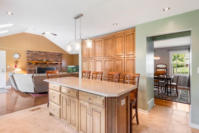 25W303 Gunston Ave, Naperville, IL 60540 - kitchen featuring a breakfast bar, a brick fireplace, lofted ceiling, a kitchen island, and light stone counters