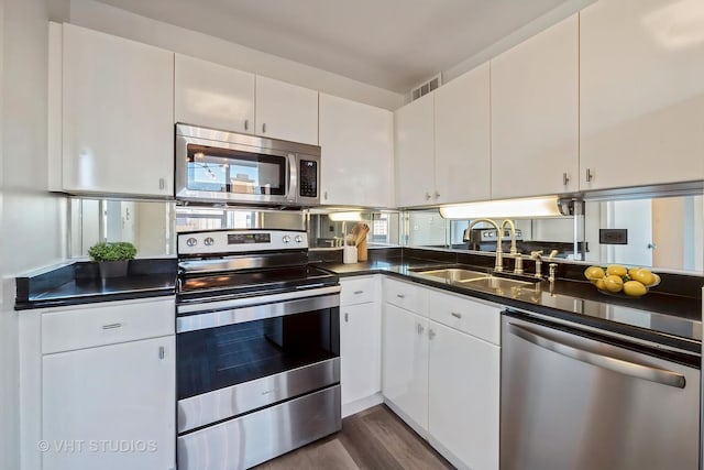 1700 E 56th St Unit 904, Chicago, IL 60637 - kitchen featuring stainless steel appliances, a sink, dark countertops, dark wood finished floors, and white cabinetry