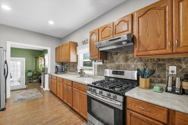 509 S Main St, Homer, IL 61849 - kitchen featuring stainless steel gas stove, under cabinet range hood, light wood-type flooring, backsplash, and brown cabinets