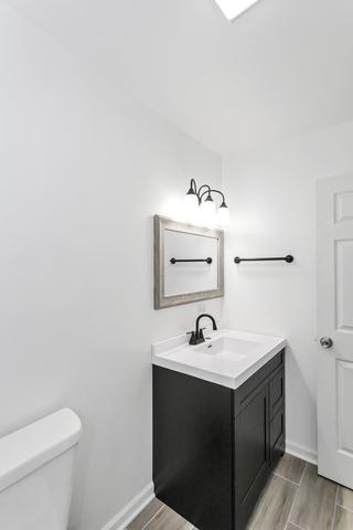 half bath with vanity, toilet, baseboards, and wood finished floors