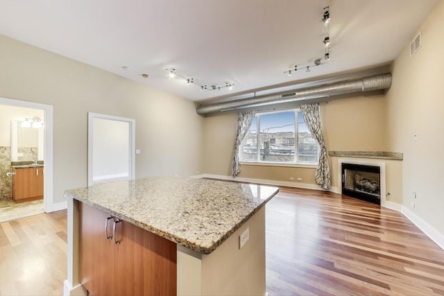 4751 N Artesian Ave Unit 206, Chicago, IL 60625 - kitchen with light wood-type flooring, a kitchen island, light stone countertops, rail lighting, and a fireplace