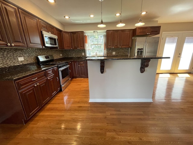 13153 W Pin Oak Dr, Homer Glen, IL 60491 - kitchen featuring appliances with stainless steel finishes, a kitchen breakfast bar, light wood-style flooring, backsplash, and decorative light fixtures