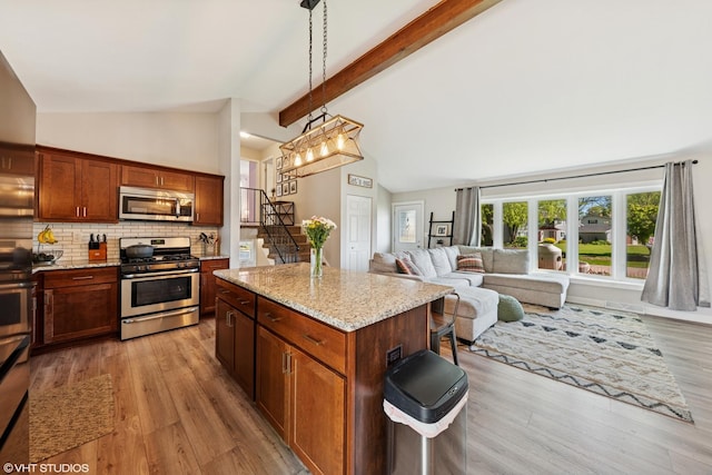2109 Sprucewood Ln, Lindenhurst, IL 60046 - kitchen with appliances with stainless steel finishes, light wood-style flooring, light stone counters, backsplash, and a center island