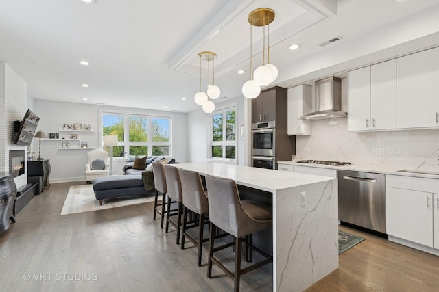 2256 W Foster Ave Unit 3, Chicago, IL 60625 - kitchen with appliances with stainless steel finishes, wall chimney exhaust hood, a kitchen island, backsplash, and wood finished floors