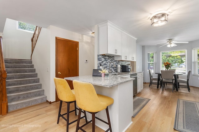 150 Meadows Ct, Sugar Grove, IL 60554 - kitchen featuring stainless steel dishwasher, light wood finished floors, white cabinetry, backsplash, and a kitchen breakfast bar