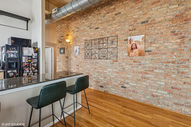 1625 N Western Unit 502, Chicago, IL 60647 - kitchen featuring brick wall, light wood finished floors, black refrigerator with ice dispenser, dark stone counters, and a breakfast bar