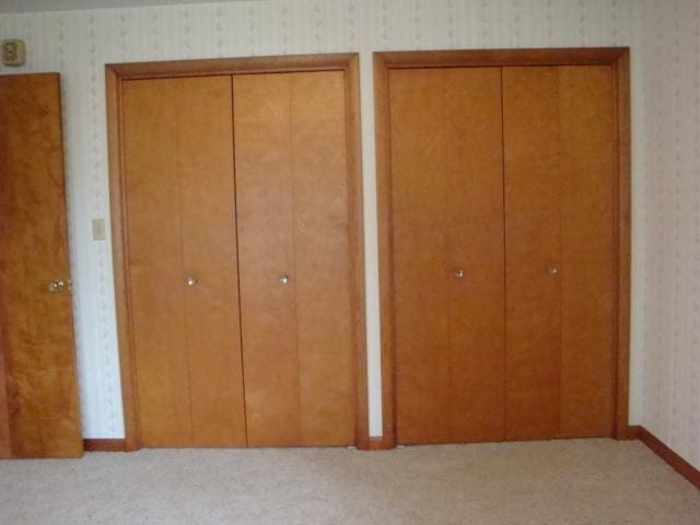 423 W Garfield Ave, Cissna Park, IL 60924 - unfurnished bedroom with wallpapered walls, two closets, and light carpet