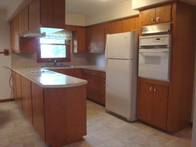 423 W Garfield Ave, Cissna Park, IL 60924 - kitchen with white appliances, a peninsula, a sink, brown cabinetry, and light countertops