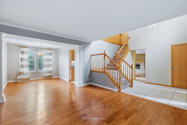 2853 Coastal Dr, Aurora, IL 60503 - unfurnished living room with a brick fireplace, light wood-style flooring, stairway, ornate columns, and ornamental molding