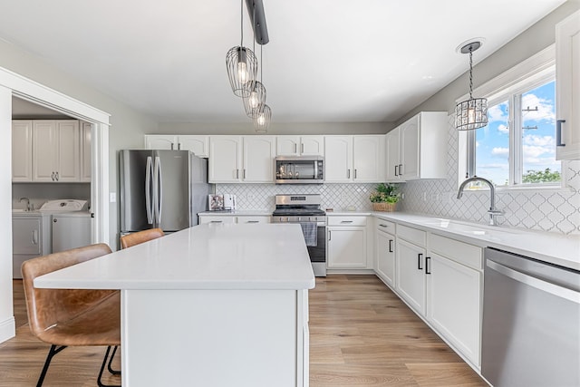 15905 Rolland Dr, Manhattan, IL 60442 - kitchen featuring stainless steel appliances, washer and clothes dryer, a breakfast bar area, a center island, and light wood-style floors