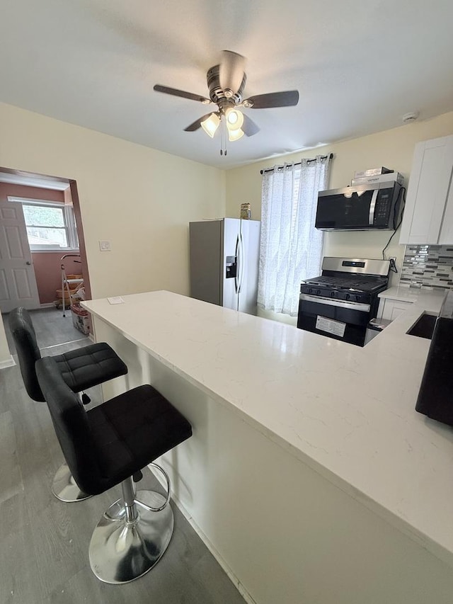 1435 S 57th Ave, Cicero, IL 60804 - kitchen with appliances with stainless steel finishes, a ceiling fan, white cabinetry, light wood finished floors, and decorative backsplash
