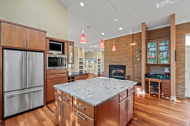 15629 W 139th St, Homer Glen, IL 60491 - kitchen featuring appliances with stainless steel finishes, brick wall, light wood-style flooring, a brick fireplace, and light stone counters